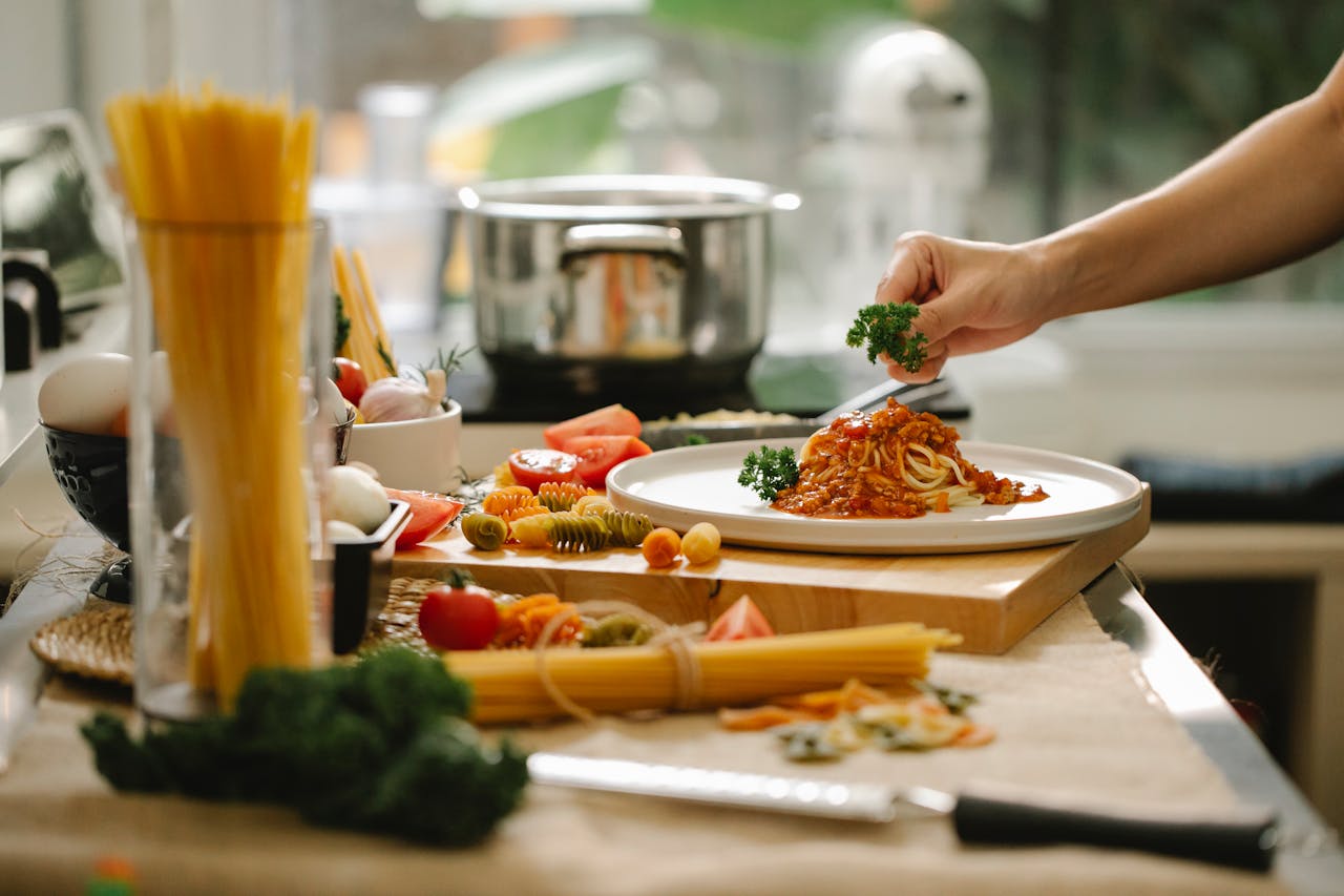 about-02 Crop anonymous chef adding parsley to spaghetti with tomato and meat while cooking lunch in kitchen